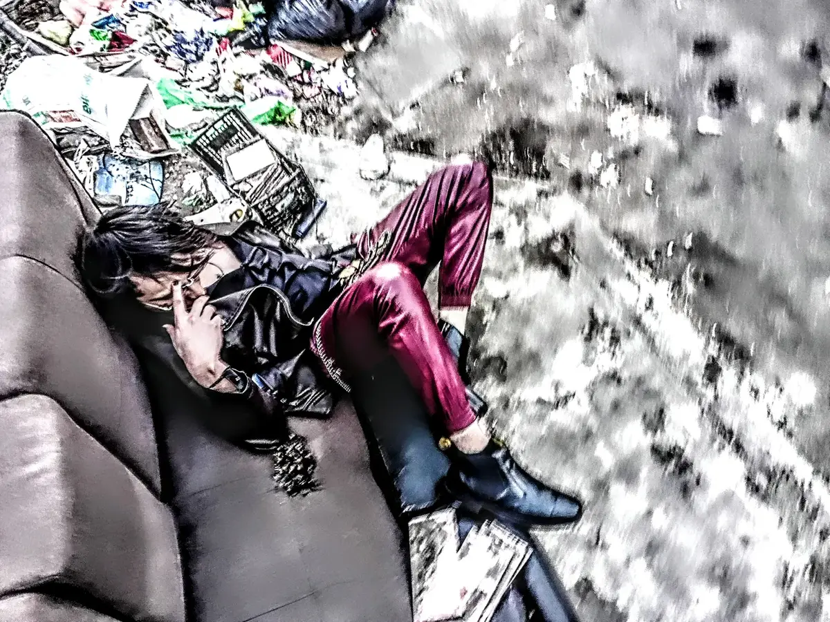 Persona recostada en un sillón abandonado entre basura