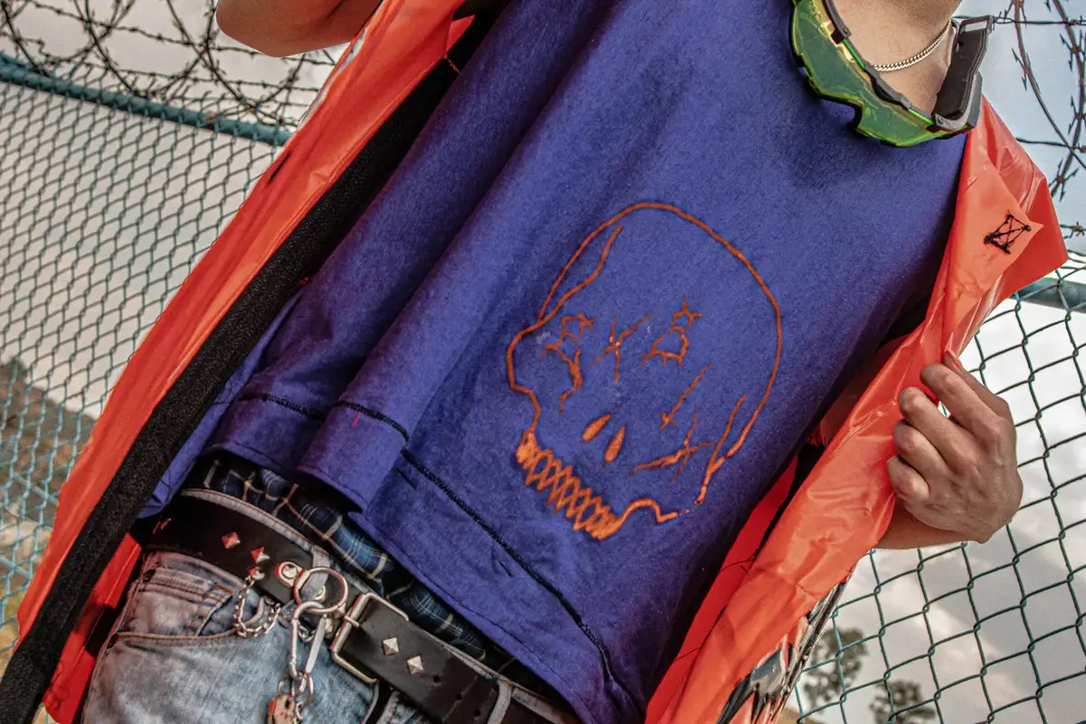 Playera morada con un cráneo estampado en naranja, bajo un chaleco naranja